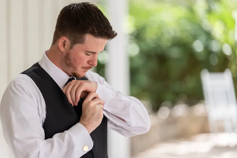 Duncan fastens his white dress shirt cuff while wearing a black vest.