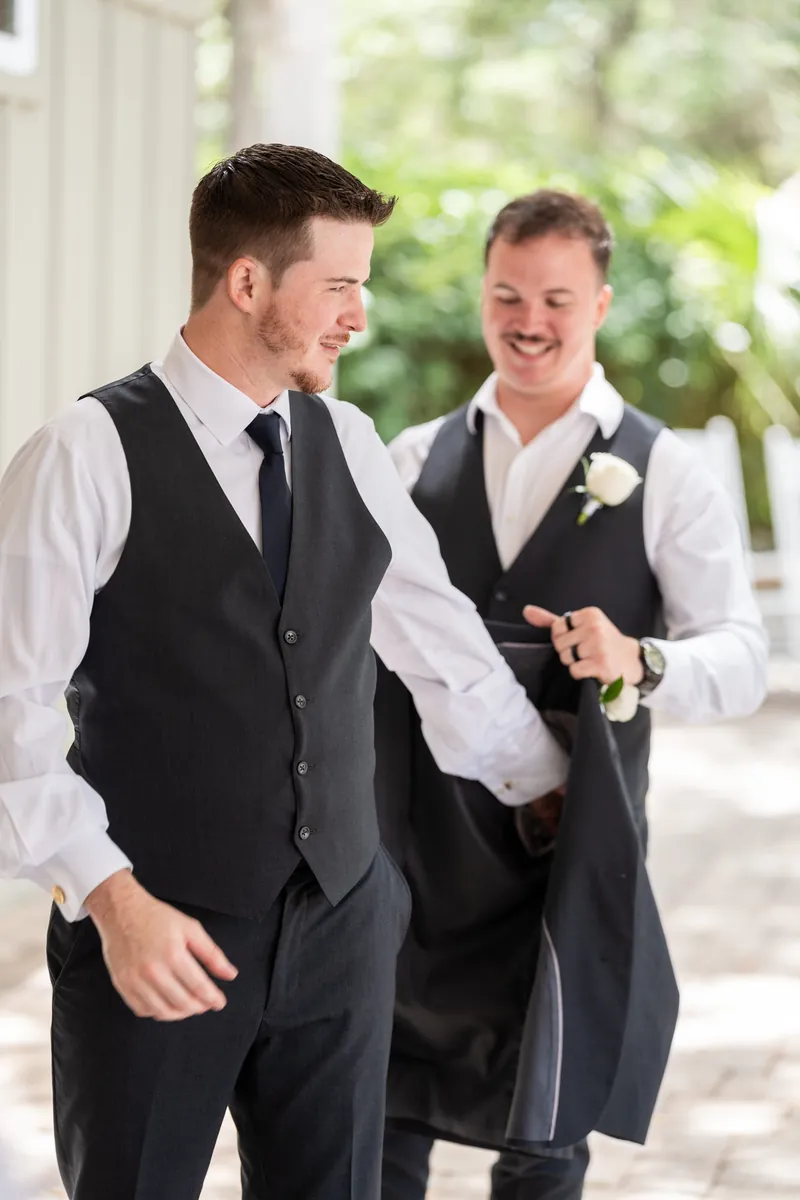 Duncan and a groomsman smile while walking together in navy suits outdoors.