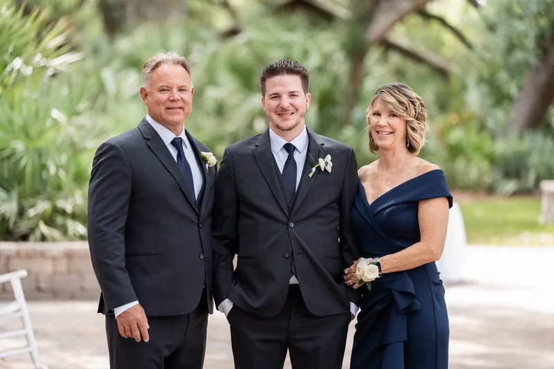 Duncan with his parents, both in dark formal attire, posed together on a brick pathway.