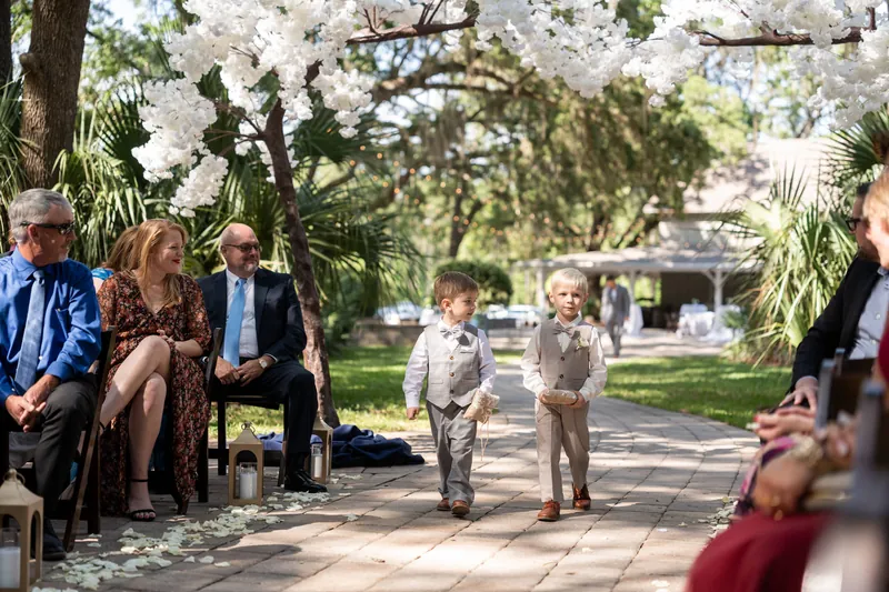 Two young boys in tan suits walk down the aisle as ring bearers while seated guests watch from both sides.