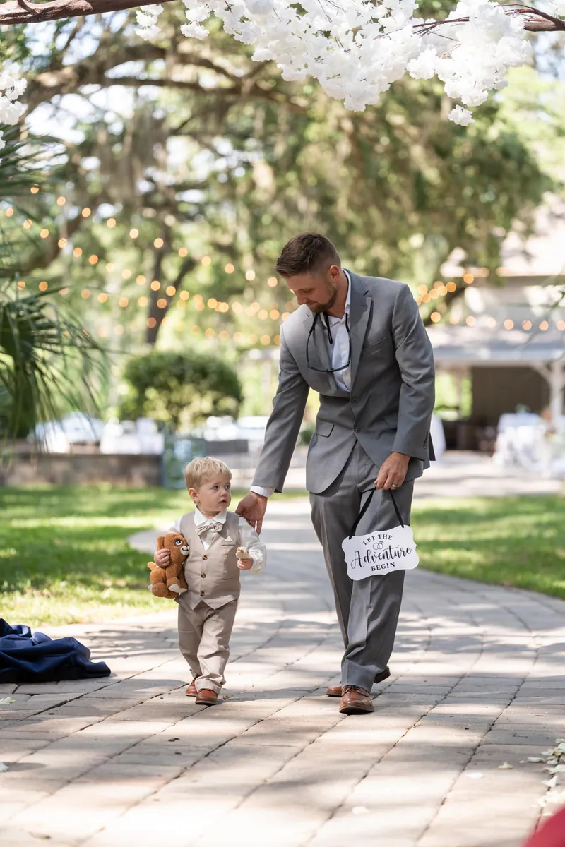 Duncan walks down the aisle with a young boy in a tan suit, both holding programs during the ceremony.
