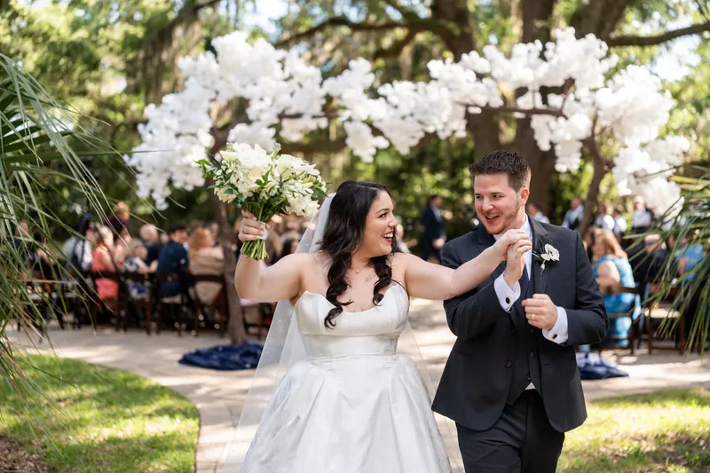 Giselle & Duncan dance joyfully under white floral arrangements at their outdoor reception.