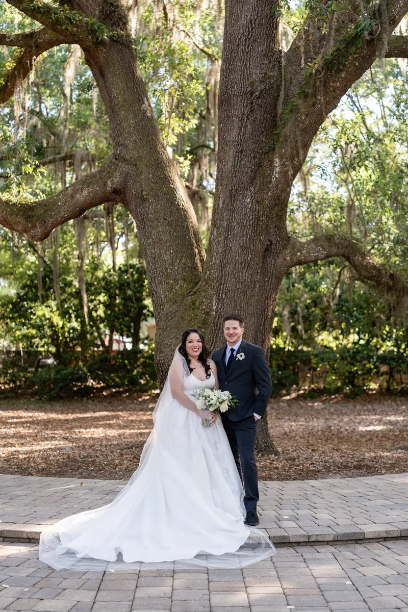 Duncan walks beside Giselle in her white gown beneath the canopy of a massive oak tree.
