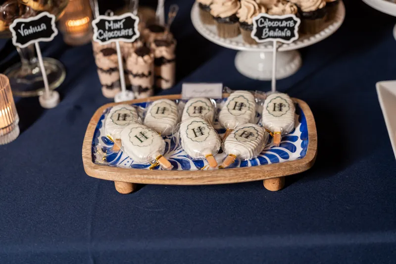 Wooden tray holding small numbered burlap pouches on navy table with chalkboard food labels and centerpieces.