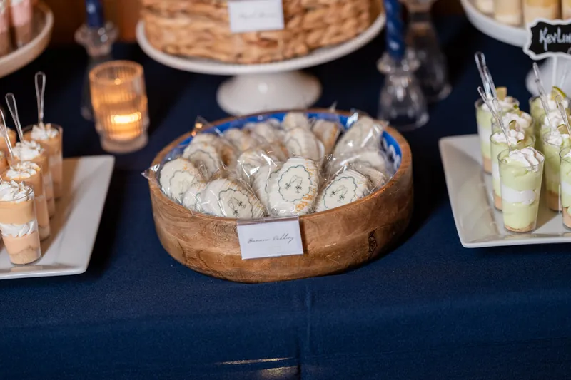 Wooden bowl of spiral pastries and green cocktails in glasses on navy table with tiered cake display.