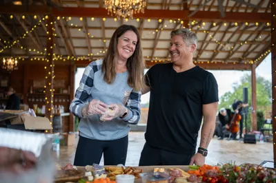 Couple smiling at food table in decorated barn venue with string lights