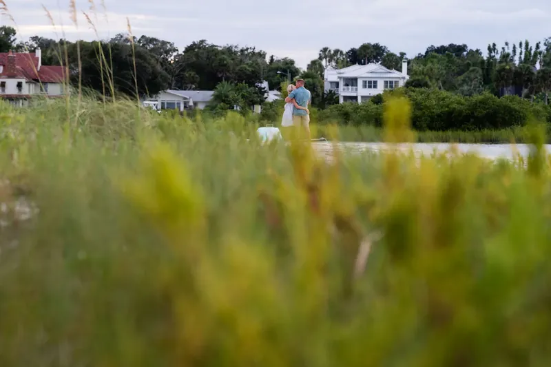 Couple embracing after proposal with sea oats in foreground