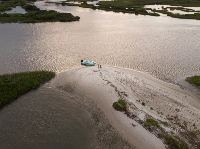 Drone view of couple on sandbar with turquoise boat