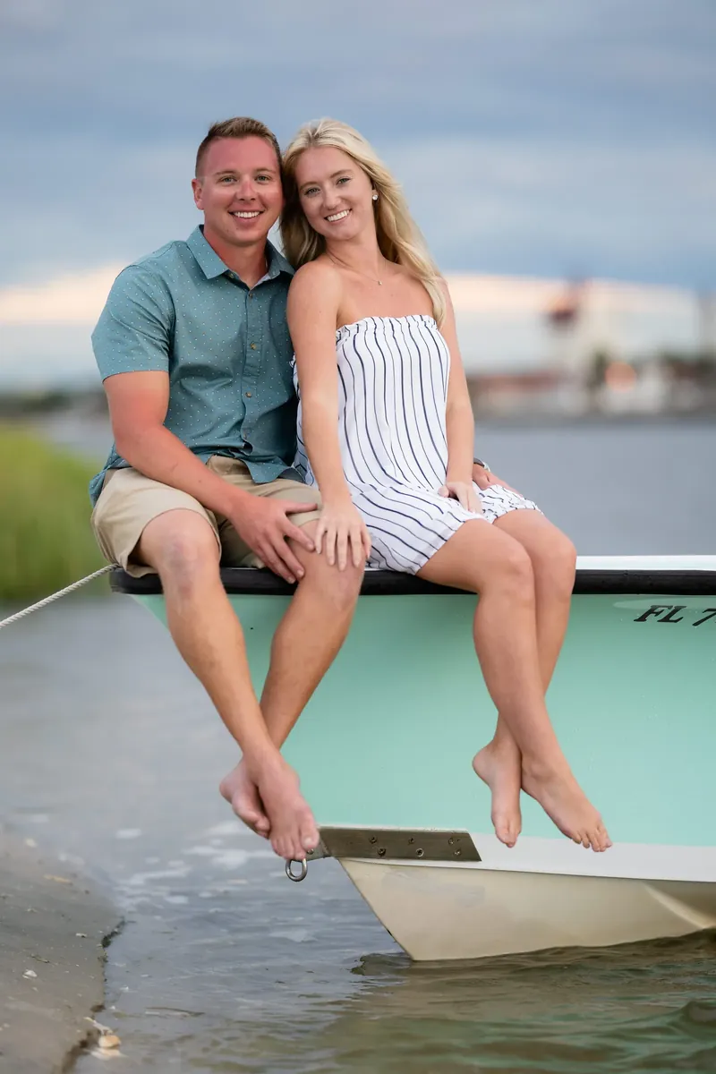 The newly engaged couple sit barefoot on the edge of a mint-green boat, feet dangling toward the shallow water at Matanzas