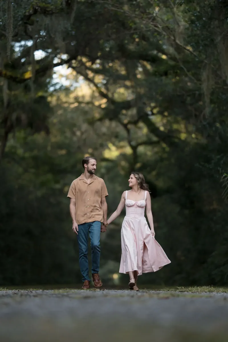 Helen and Saje walking hand in hand under the oak canopy