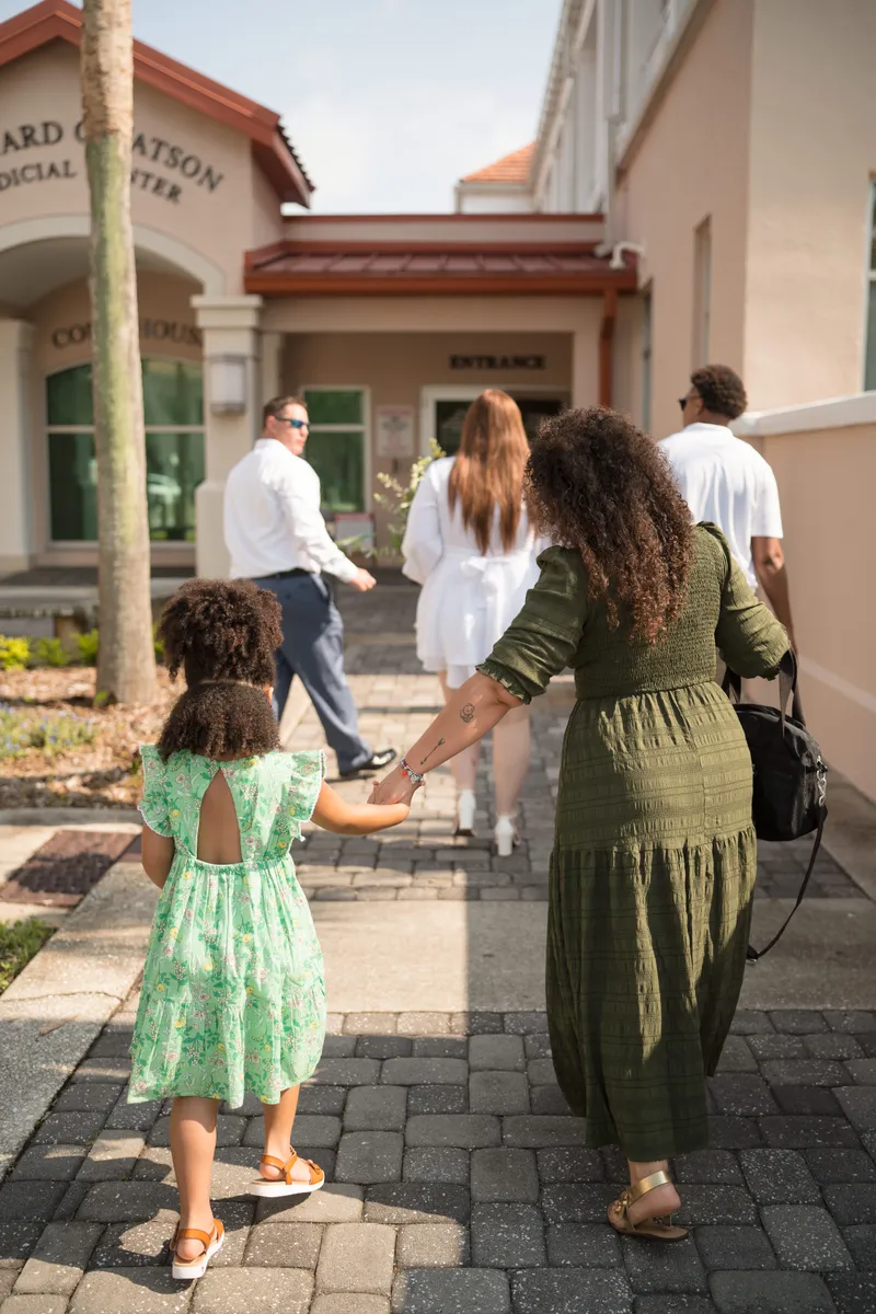 A family walks together toward the courthouse entrance for an intimate elopement ceremony, with a young child in a green dress holding hands with her mother.