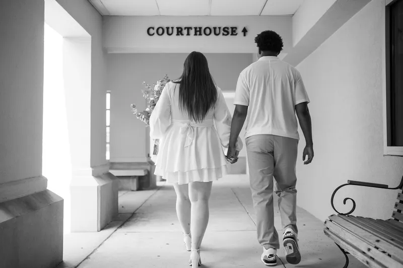 A couple walks hand in hand down a courthouse hallway toward their intimate elopement ceremony, captured in romantic black and white.