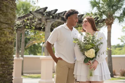 Couple smiling together in elegant garden with white flowers and pergola