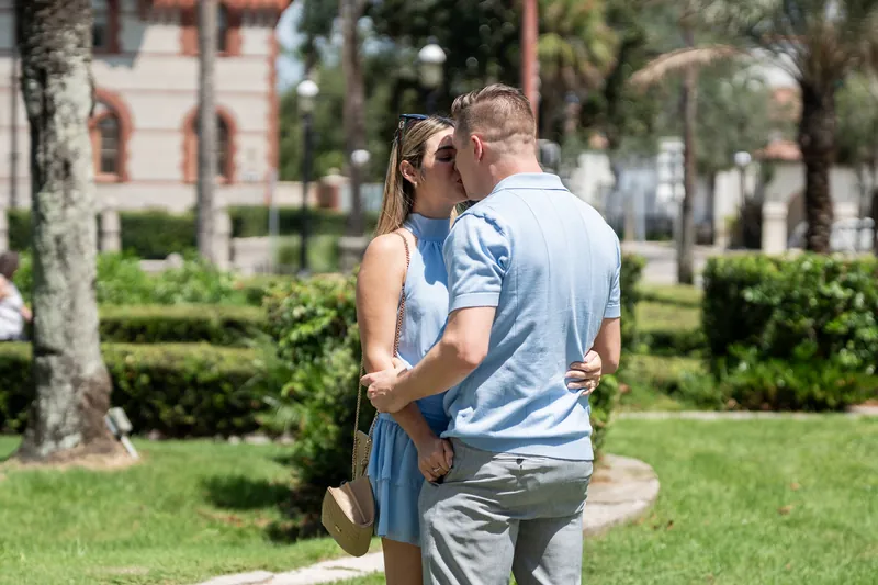 Jakub lifts Josy off the ground in a grassy courtyard lined with palm trees and manicured hedges.
