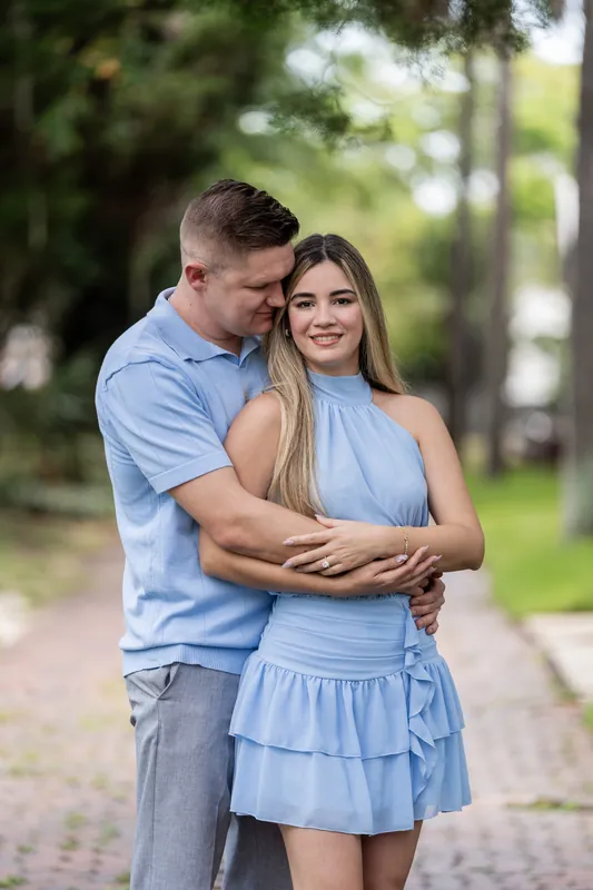 Jakub embraces Josy from behind on a tree-lined brick pathway in Downtown St Augustine, both wearing light blue.