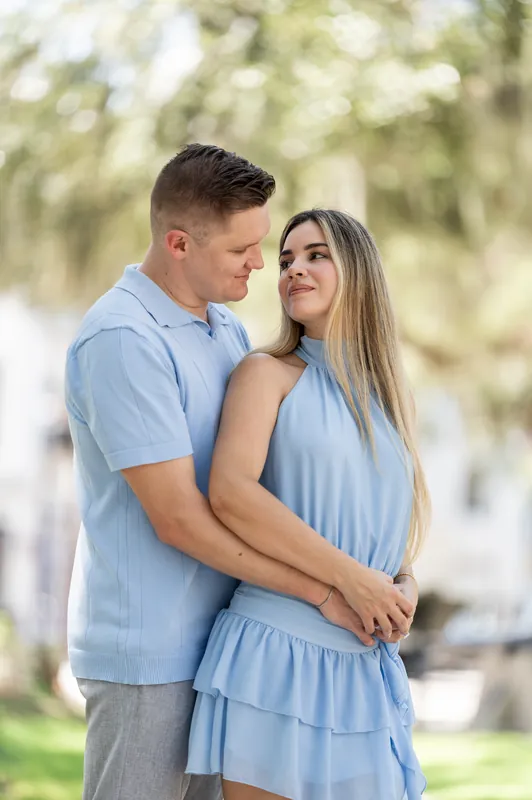 Josy smiles at Jakub as he wraps his arms around her from behind on a tree-lined street.
