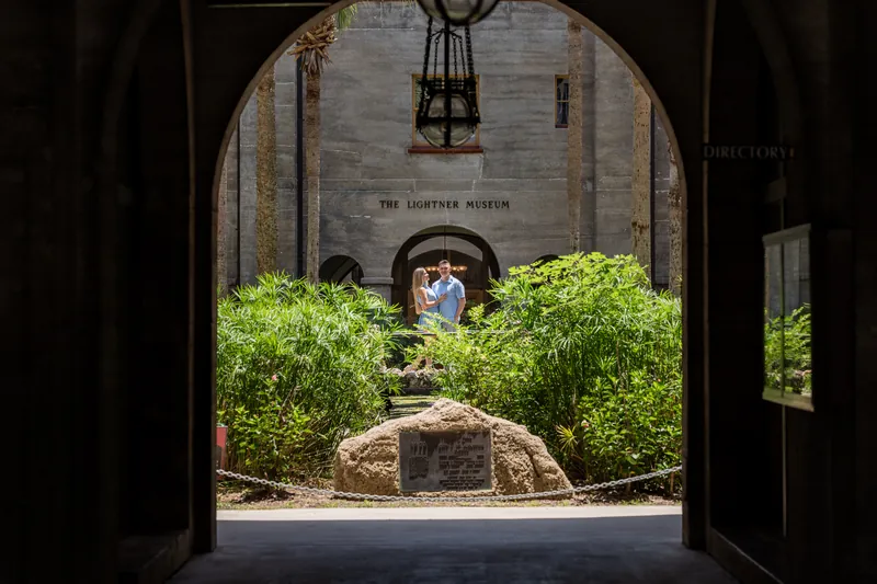 Jakub and Josy stand together under a stone archway surrounded by lush green shrubs in Downtown St Augustine.
