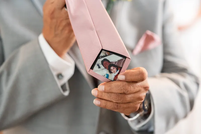 Rick holds a pink ribbon with a photo pendant of Janet during their first look moment.