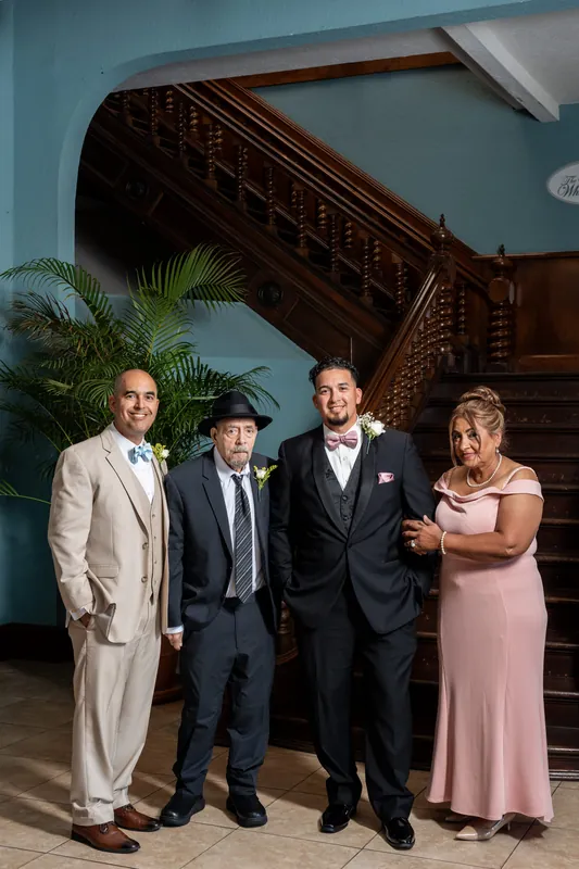 Rick stands with family members in formal attire near an ornate wooden staircase at the venue.