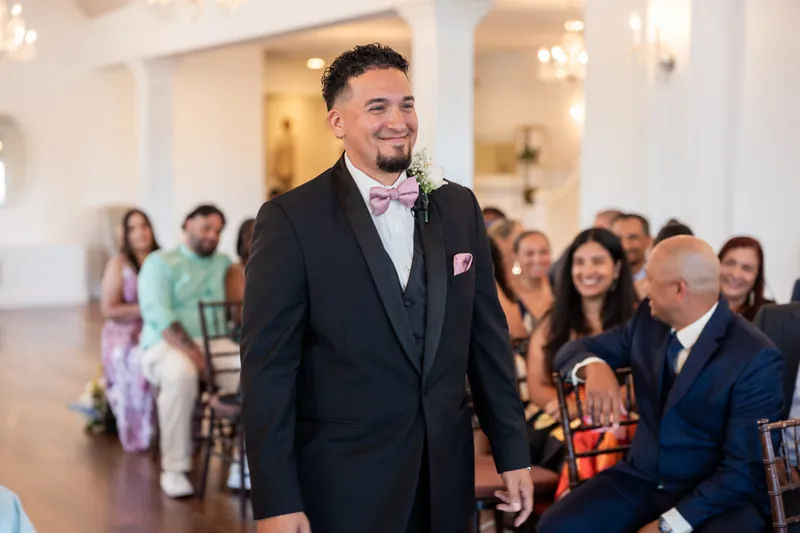 Rick smiles while standing in the elegant reception hall surrounded by seated guests in formal attire.