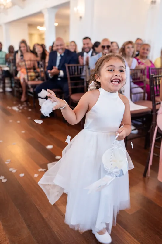 A flower girl in a white dress laughs and twirls down the aisle scattering petals during the ceremony.