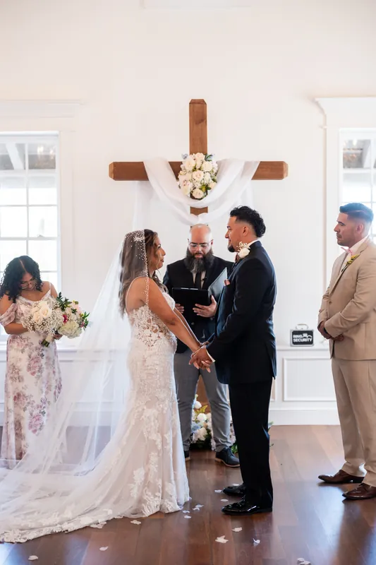 Rick and Janet face each other at the altar with an officiant between them and a wooden cross overhead.