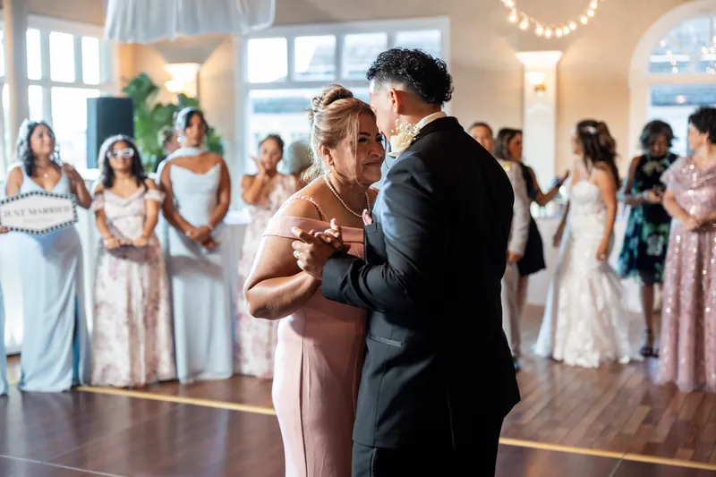 Rick and a female guest dance together as Janet looks on, surrounded by formally dressed attendees.