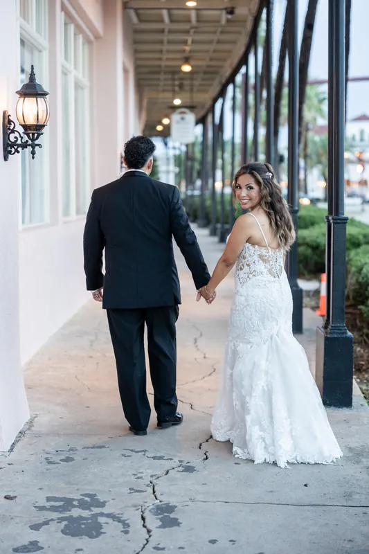 Janet and Rick hold hands while walking down a brick-lined street in downtown St. Augustine, she in a white lace gown and he