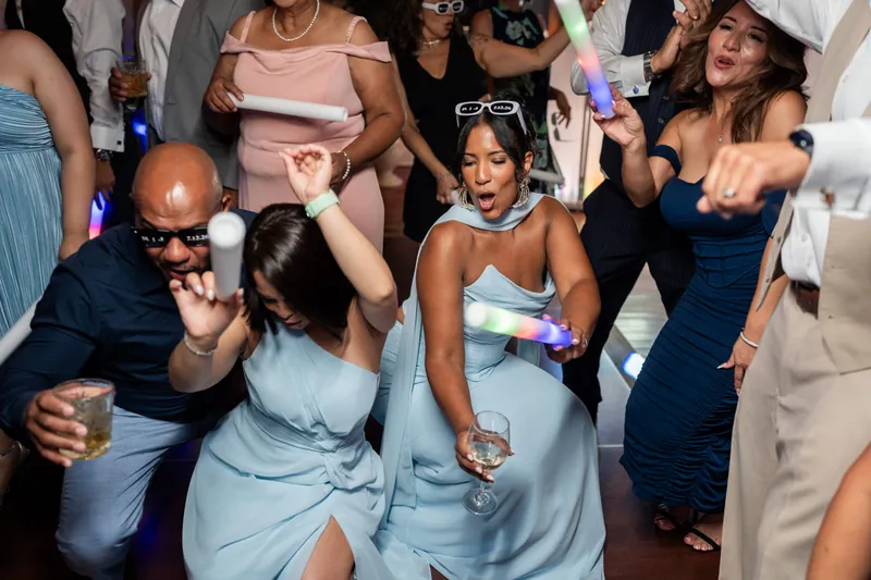 Guests dance energetically on the reception floor, including children and adults in formal and pastel attire.