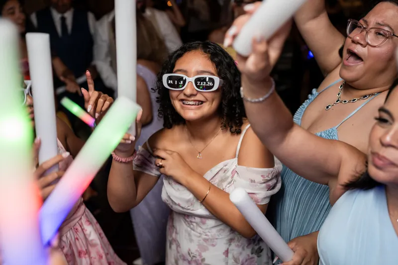 A guest wearing sunglasses dances joyfully among other wedding attendees during the evening celebration.