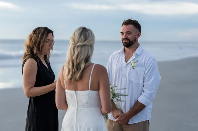 Brandon holds Jarah's hand as their officiant speaks during the beach vows at sunset.
