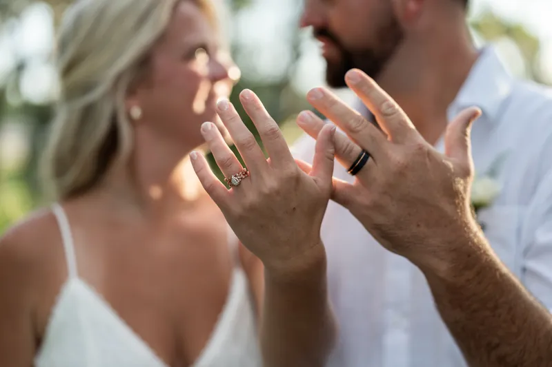 Their hands meet in the center frame, displaying matching wedding bands under dappled sunlight.
