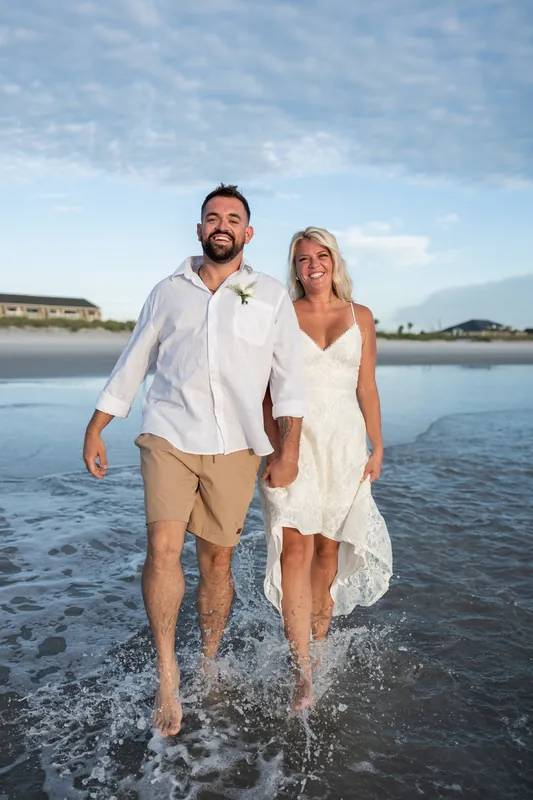 Brandon and Jarah stand on a shaded path lined with oak trees at Mussallem Beachfront Park, holding hands and smiling.