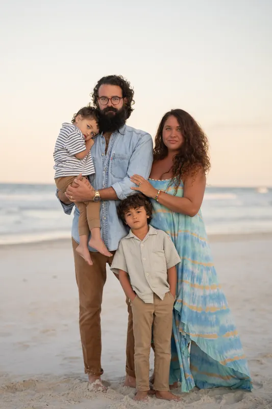 Two adults and two children stand on the sand at St. Augustine Beach at sunset, with one adult holding a young child.