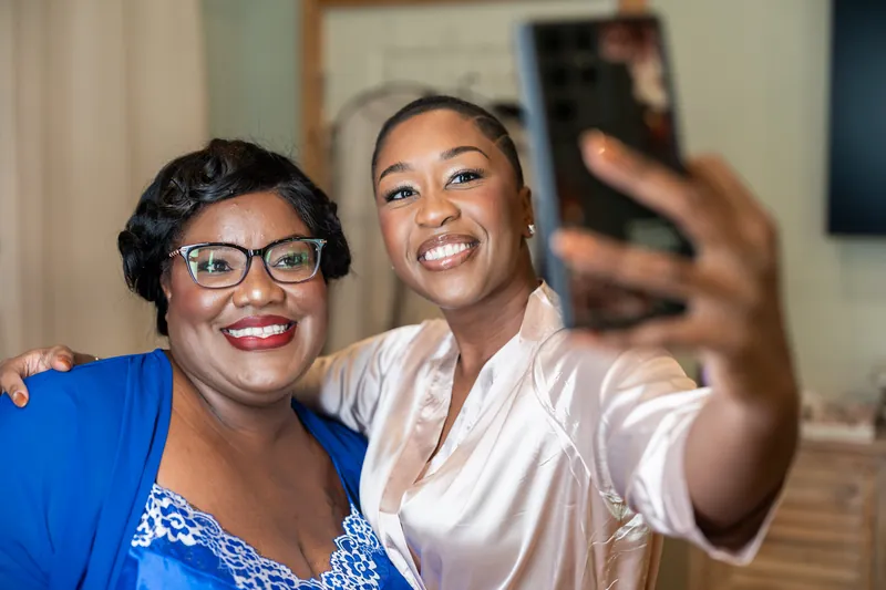 Two people in blue and white clothing smile while taking a selfie indoors near a framed mirror.