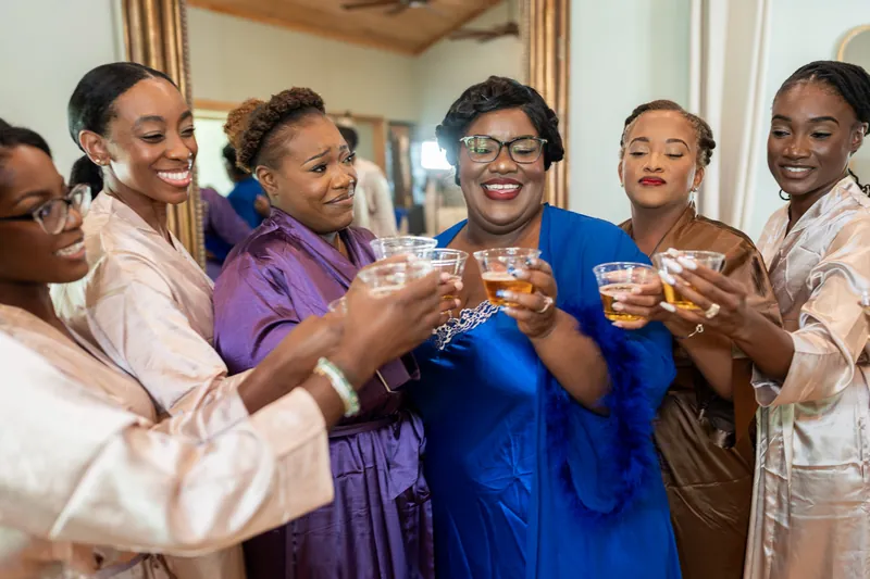 Jazzalynn and five others in robes clink glasses together indoors, smiling and celebrating.
