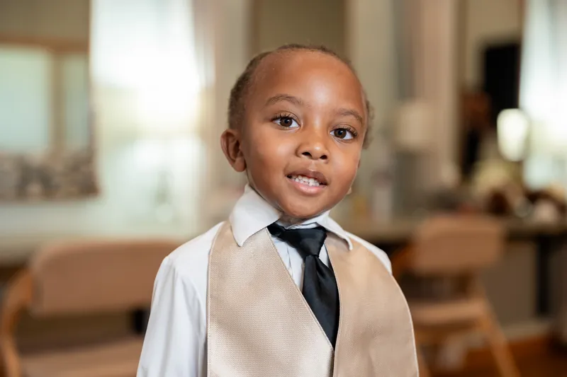 Young child in cream vest and black tie stands indoors at Fountain of Youth Archaeological Park.