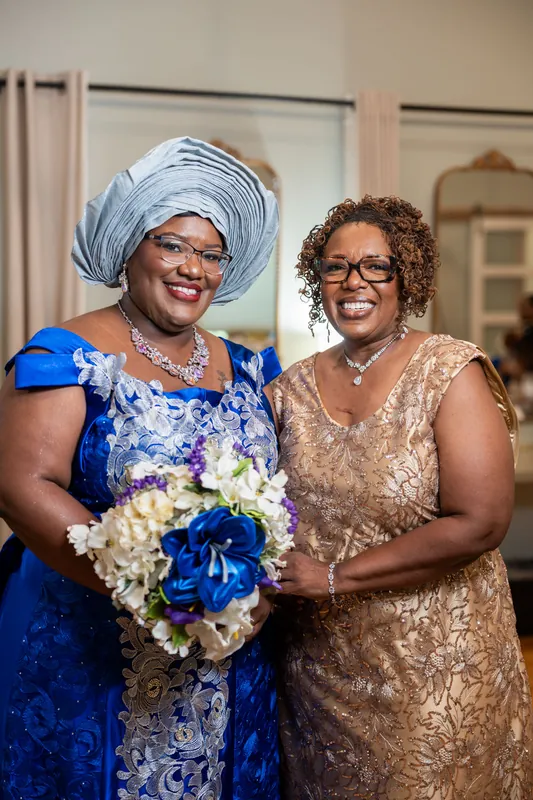 Two women smile together holding a bouquet of white and blue flowers at the venue.
