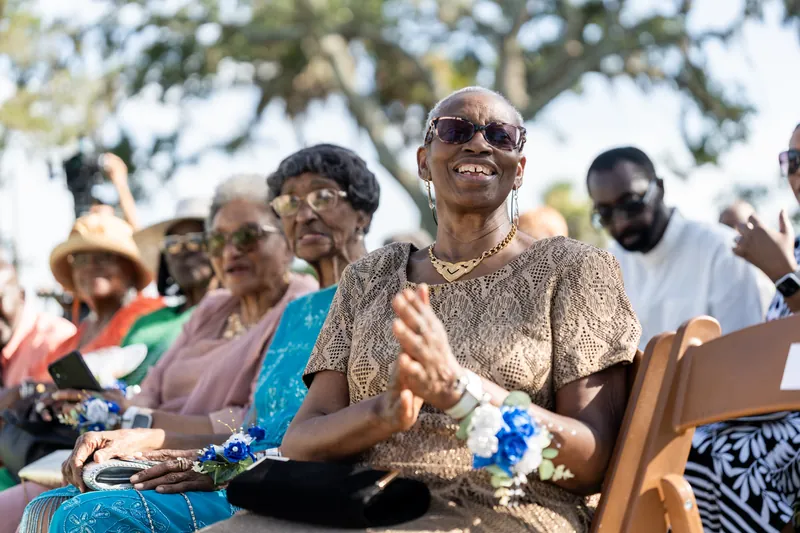 Guests seated under oak trees smile and applaud during an outdoor ceremony at Fountain of Youth Archaeological Park.