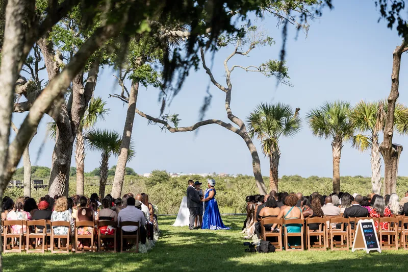 Wedding guests sit in rows facing the couple under sprawling oaks with Spanish moss and palm trees in the background.