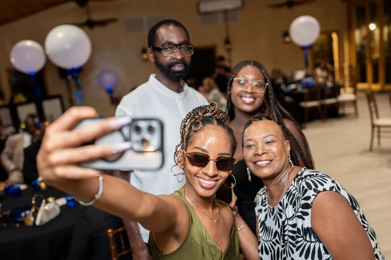 Four guests take a selfie together indoors, with two wearing sunglasses and smiling at the camera.