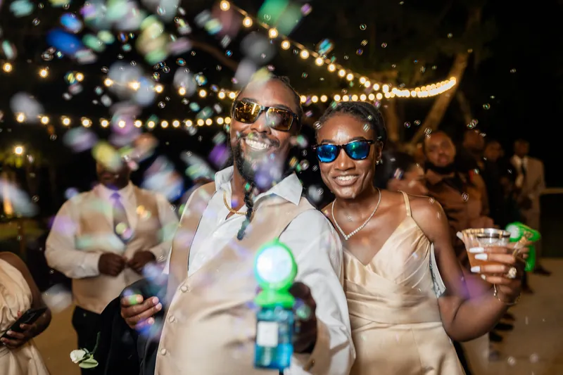 Hakeem and a guest in cream-colored outfits enjoy the outdoor reception under twinkling lights and floating bubbles.