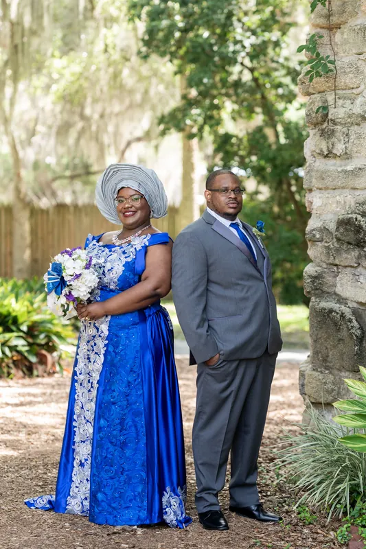 Jazzalynn in a blue dress with white headwrap and Hakeem in gray suit pose by a stone wall at Fountain of Youth