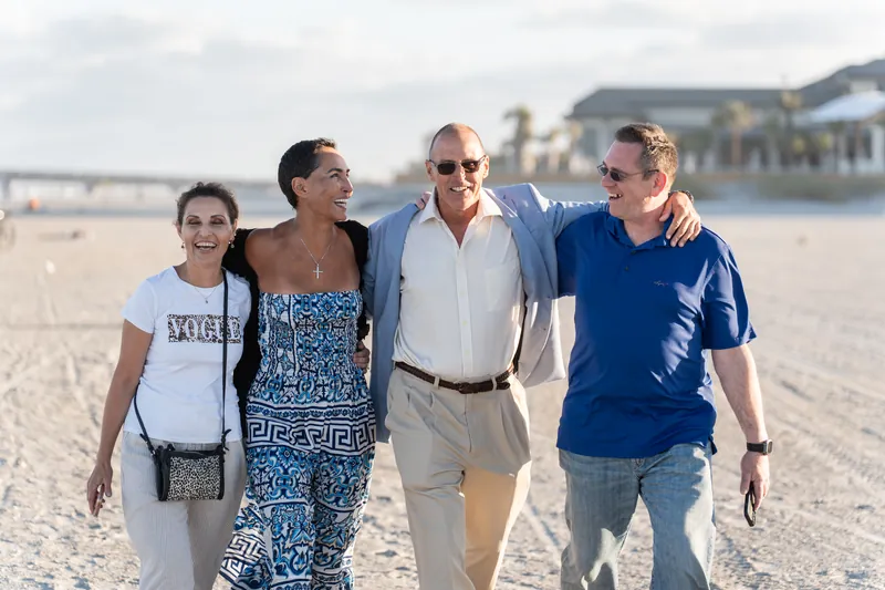 Four people walk together along the beach at St. Augustine Beach, smiling and enjoying the moment with the water and skyline behind them.