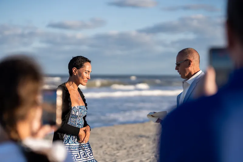Onlookers blur in the foreground while the couple exchanges a look during their beachside proposal.