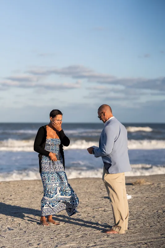 Jeff and Ella stand face-to-face on the sand at St. Augustine Beach, waves rolling behind them as he extends his hand in proposal.