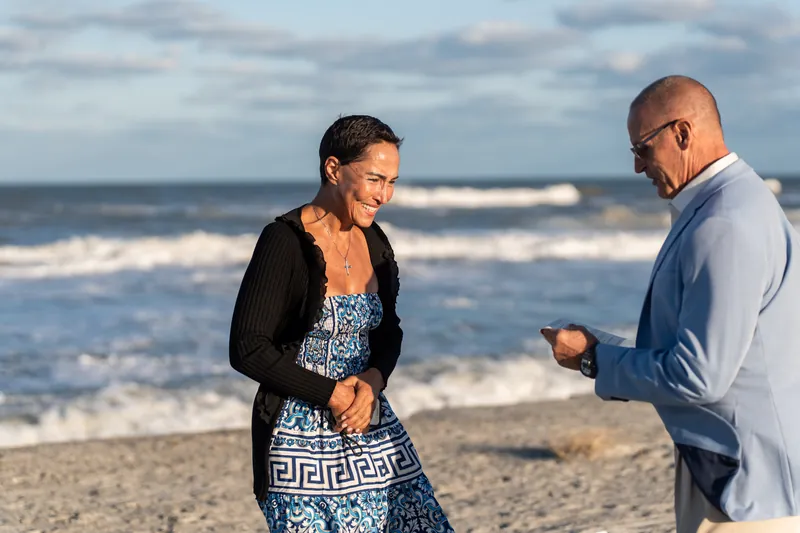 Ella gazes at Jeff with her hand over her heart as he kneels on the beach at St. Augustine, the Atlantic Ocean and cloudy sky framing the moment.