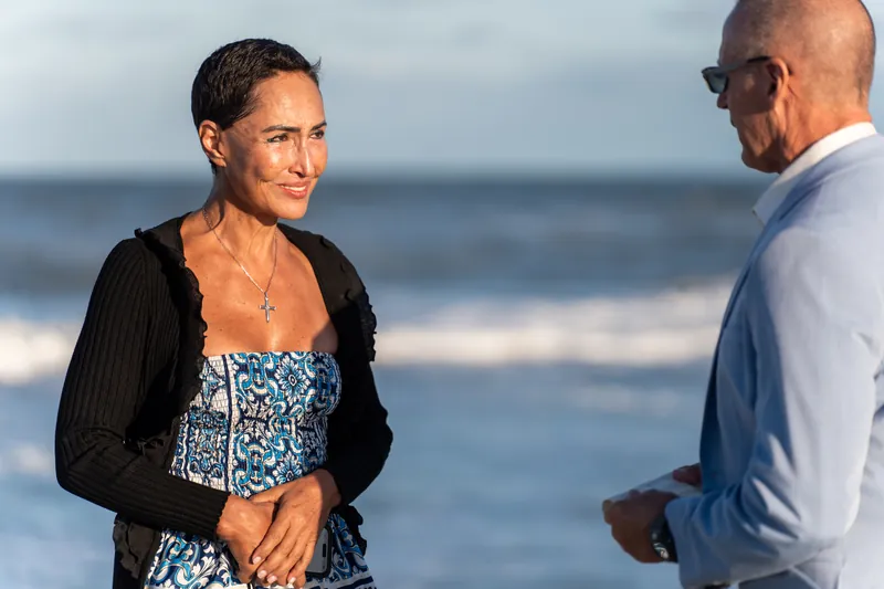 Close-up of Ella's emotional expression as Jeff holds an open ring box during their proposal at St. Augustine Beach, the ocean visible behind them.