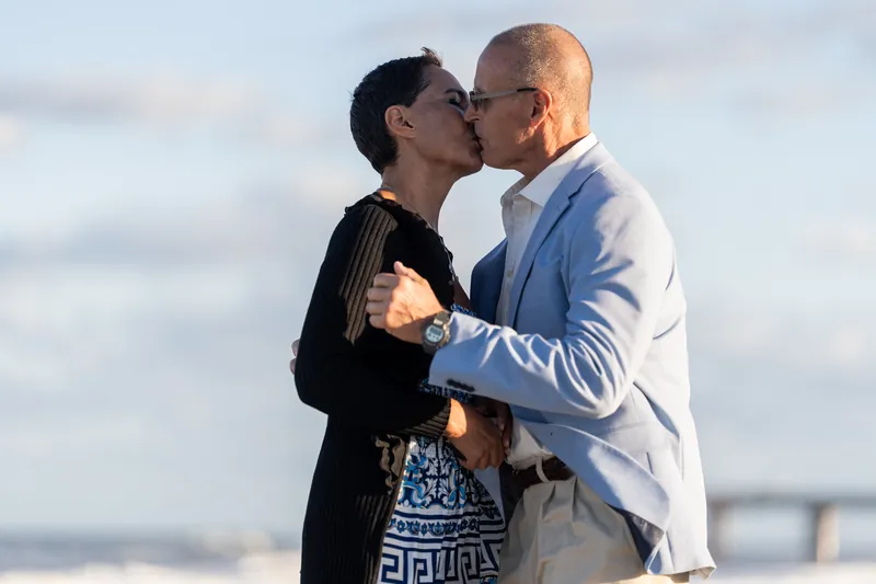 The newly engaged couple embrace and kiss on the shoreline at St. Augustine Beach, the surf and sky soft behind them.