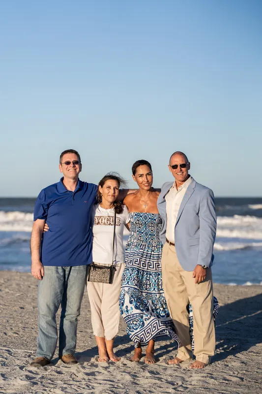 Four adults pose together on the sand at St. Augustine Beach with the Atlantic Ocean and breaking waves behind them.